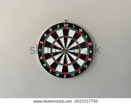 The arrow board which is dominated by black, white, green and red colors is attached to the wall. Focus on the red dot in the center and reach the target that has been prepared