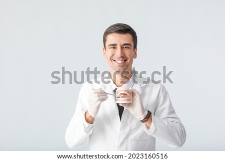 Male dentist with plastic jaw model on light background Royalty-Free Stock Photo #2023160516
