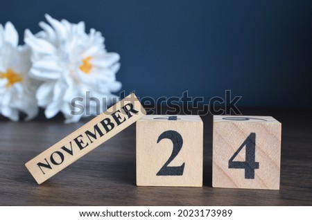 November 24, Date cover design with calendar cube and white Paeonia flower on wooden table and blue background.
