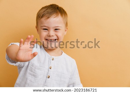 White boy with down syndrome smiling and gesturing at camera isolated over beige background Royalty-Free Stock Photo #2023186721