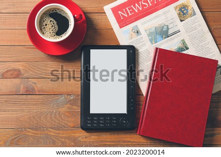 E-reader, book, newspaper and cup of coffee on wooden background