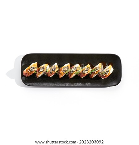 International sushi roll topped with smoked eel and sesame seed. Sushi roll with avocado and crab meat inside. Black slate sushi plate isolated on white background. Delicious sushi restaurant menu