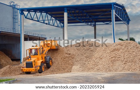 Front loader loading wood chips in pile in warehouse. Loader works at wood chips storage yard. Alternative ecological fuels. Sawdust processing, woodchip biomass heap. Pellets manufacturing Royalty-Free Stock Photo #2023205924