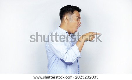 Asian Indonesian businessman in blue shirt with angry expression pointing. isolated on a white background with side copy space. Royalty-Free Stock Photo #2023232033