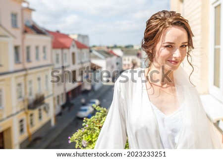 young beautiful girl bride in a peignoir standing on the balcony overlooking the old town and waiting for the groom