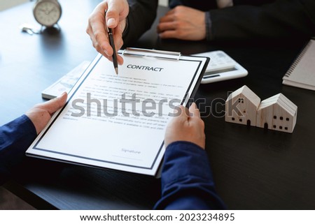 Real estate agents show miniature house models to the customers and calculate house prices on the table with a key, house design document. Business Signing a Contract Buy or sell concept
