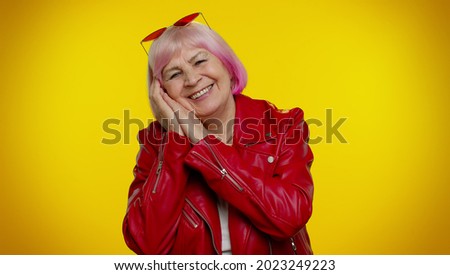 Elderly granny woman with pink hair yawning, sleepy inattentive feeling somnolent lazy bored gaping suffering from lack of sleep. Senior old grandmother isolated on yellow background. People emotions