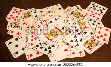 deck of playing cards such as poker or rummy, randomly scattered on a dark brown wooden game table