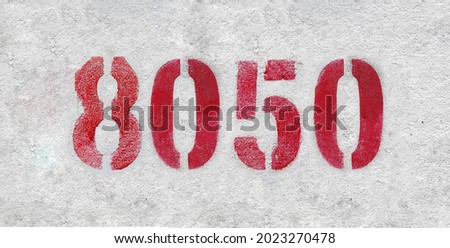 Red Number 8050 on the white wall. Spray paint. Number eight thousand and fifty.