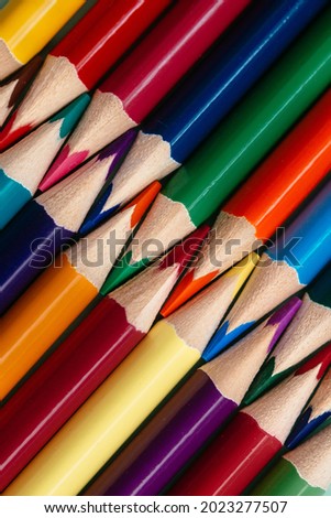 Colored sharpened pencils lie in a row close-up. Solid abstract background of wooden multi-colored pencils. These are school supplies.