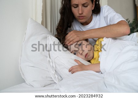 Mother taking care of sick son check kid temperature touch forehead with hand. Unwell unhealthy boy lying in bed under blanket suffer from seasonal flu or coronavirus illness at home. Child healthcare Royalty-Free Stock Photo #2023284932