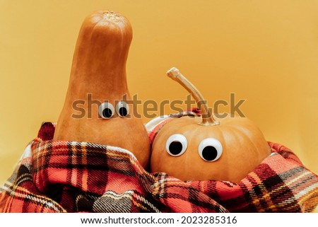 Pumpkin with googly eyes in warm red scarf, warm autumn concept, yellow background with copy space.