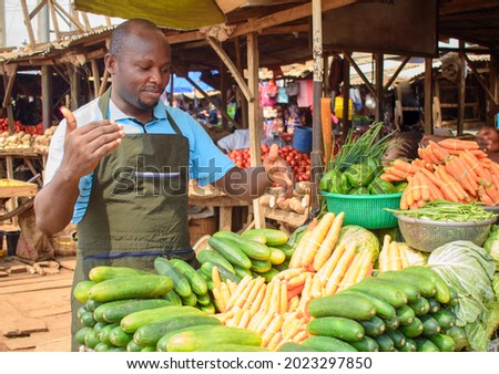 stock photo of male African grocery seller or business man with apron, standing at his stall in a market, ready to sell to customers