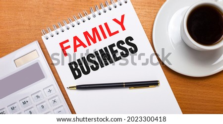 On a wooden table there is a white calculator, a white cup of coffee, a pen and a white notebook with the text FAMILY BUSINESS. Business concept