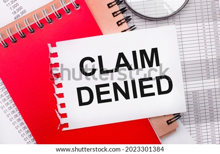 On a light background - reports, a magnifying glass, brown and red notepads, and a white notepad with the text CLAIM DENIED. Business concept