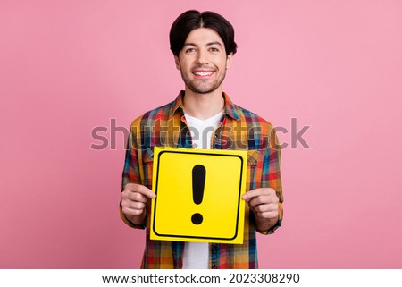 Photo of pretty charismatic young guy dressed checkered clothes smiling holding exclamation point card isolated pink color background