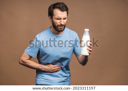 Young man in pain holding his hurting stomach isolated on beige background. Abdominal pain. Lactose milk intolerance. Royalty-Free Stock Photo #2023311197