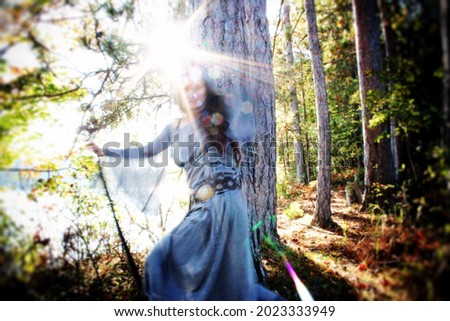 Medieval woman in whirling motion by a misty early morning lake. Green Witch or Shamanic story. She is holding a staff within lens flare and evokes powerful energy. Royalty-Free Stock Photo #2023333949