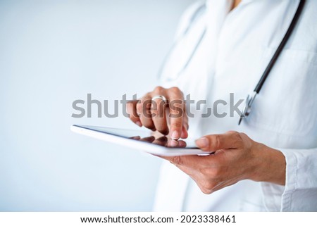 Female doctor using her digital tablet in the office. Close-up of a female doctor using tablet PC. A picture of a doctor holding tablet over white background. Hands holding medical report, copy space.