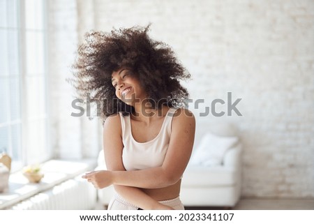 A satisfied mixed-race woman enjoys rhythmic movement. A cheerful young black lady dancing and enjoying a carefree weekend at home while relaxing in her apartment, listening to music, no stress. Royalty-Free Stock Photo #2023341107