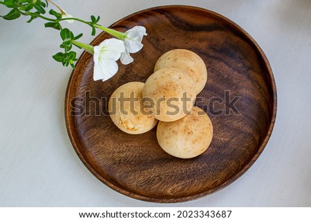 Fresh homemade round cookies (mini buns) on a dark wood plate. There's a white flower in the corner