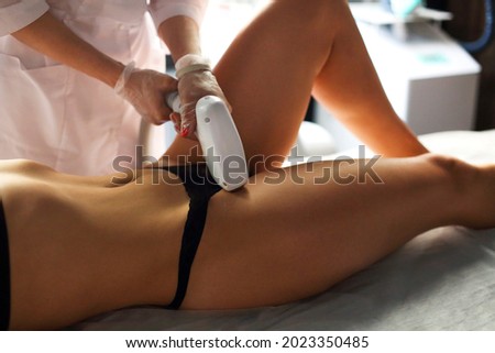 Cropped shot of beautician in medical uniform and gloves making laser hair removal procedure of bikini zone to young slender relaxed woman in black underwear. Body care treatment concept