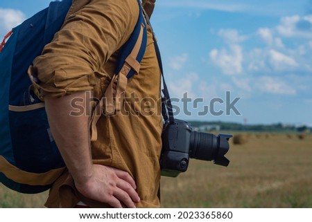 Traveler photographer with a camera in his hand against the background of a field and haystacks