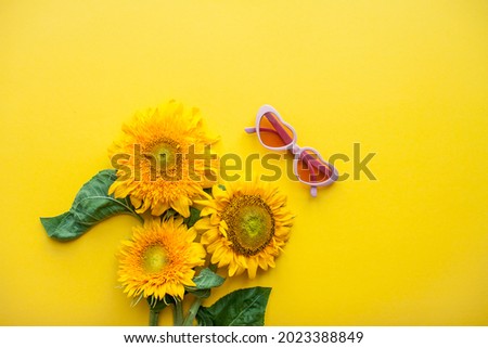 Arrangement of pink sunglasses in the shape of hearts and sunflowers on a bright yellow background