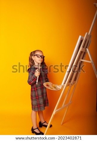 European girl on a yellow background with a brush and a palette of paints in her hands draws a picture on an easel. Creativity, thoughtfulness, joy.

A girl in a school uniform thinks about looking fo