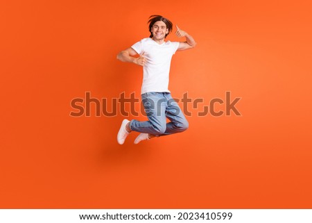 Full length photo of young happy positive man jump up make thumb up smile isolated on orange color background