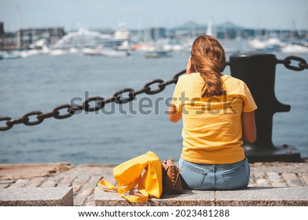 Woman sitting, watching the view Boston skyline and Sailboat seen from Piers Park, Massachusetts, USA