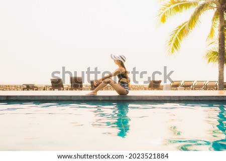 Portrait beautiful young asian woman relax around outdoor swimming pool in hotel resort with palm tree at sunset or sunrise for leisure vacation