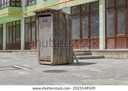 Wooden toilet on the street, background of a modern house. 