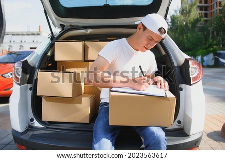 Young male courier with parcels near delivery service car