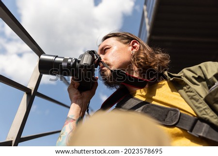 Working day of photographer. Portrait of young man, cameraman with professional camera, equipment during summer day outdoors. Concept of occupation, job, education, caree and hobby