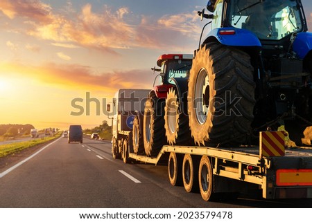 POV heavy industrial truck semi trailer flatbed platform transport two big modern farming tractor machine on common highway road at sunset sunrise sky. Agricultural equipment transportation service Royalty-Free Stock Photo #2023579478