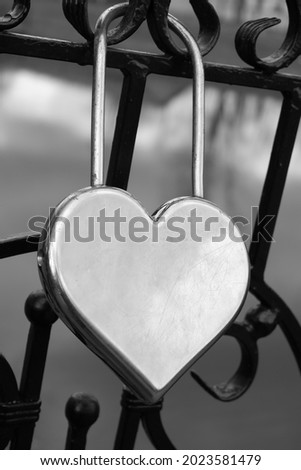 Metal silver door lock in the shape of a heart on the fence as a symbol of eternal love.