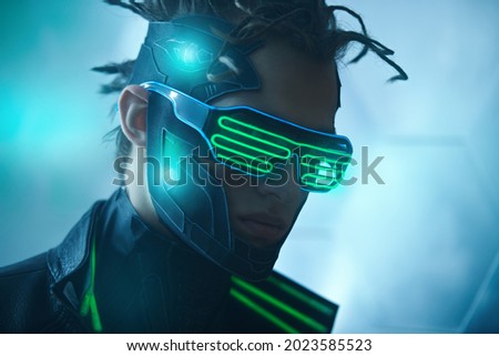 Close up portrait of cyberpunk warrior of the future in green virtual reality glasses on blue digital background. Game, virtual reality. Future technologies. Royalty-Free Stock Photo #2023585523