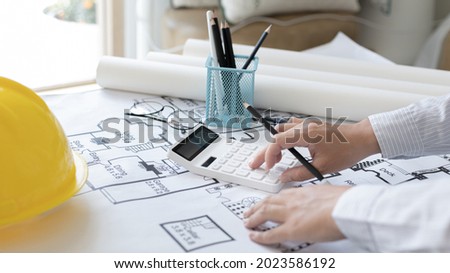 Male engineer or architect is pressing a calculator to calculate the building's structure and balance, Architects or engineers are designing buildings using calculator to calculate the physical. Royalty-Free Stock Photo #2023586192