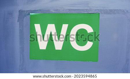 Big sign WC with white letters on green paper sticker on building wall at city street
