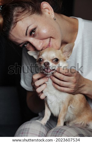 Pretty mature woman with Chihuahua dog on dark sofa in home living room. Middle aged female and her doggy Chihuahua. Concept pet love and family friend