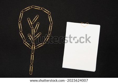 Stack of paper fastened with a golden paper clip in the shape of a heart and a tree made of paper clips on a black background. Mockup for your text.