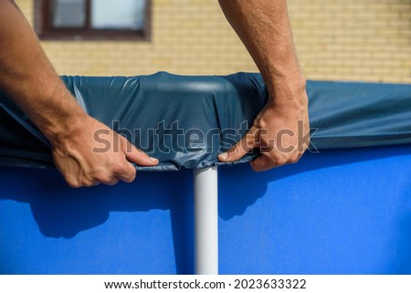 A man pulls up an cover over a home swimming pool. Debris protection Royalty-Free Stock Photo #2023633322