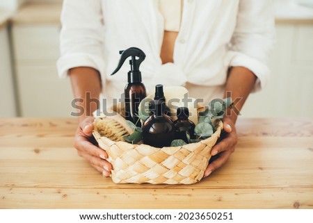 Woman holding wicker basket with natural eco-friendly zero waste plastic free cleaning items: brushes, rugs, soap, essential oils, spray and sponges at the kitchen. Plastic free home. Royalty-Free Stock Photo #2023650251