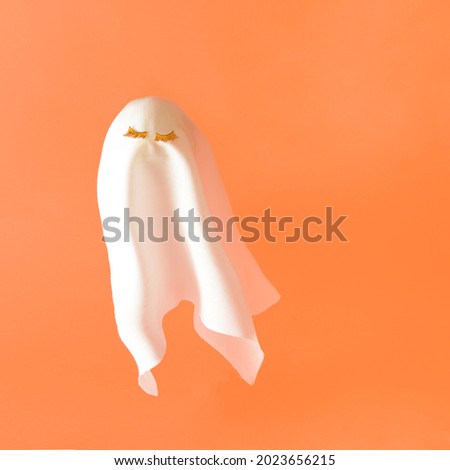 White ghost costume with gold lashes flying on a orange background. Halloween minimal composition.