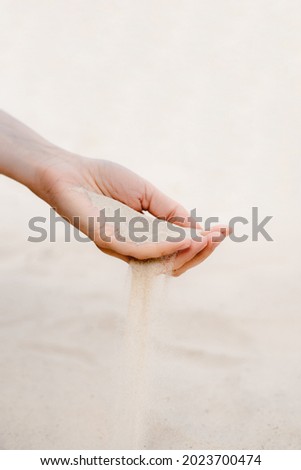 White sand pours through the fingers of a woman's hand.