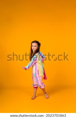 a little girl in a plush costume dances on a yellow background with a place for text