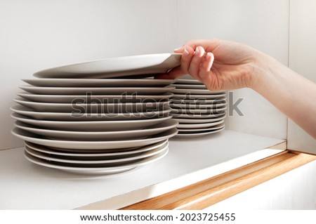 Fingers picking up a plate from a stack in the cupboard Royalty-Free Stock Photo #2023725455