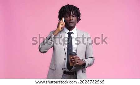 African american businessman holding paper cup and talking on cellphone isolated on pink