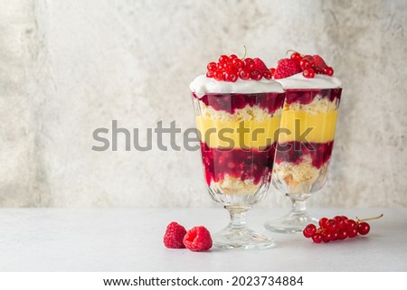 Individual size Trifles, layered dessert in glass with berry jelly, custard,  sponge and whipped cream, decorated with fresh red currant and raspberry. Copy space. Royalty-Free Stock Photo #2023734884